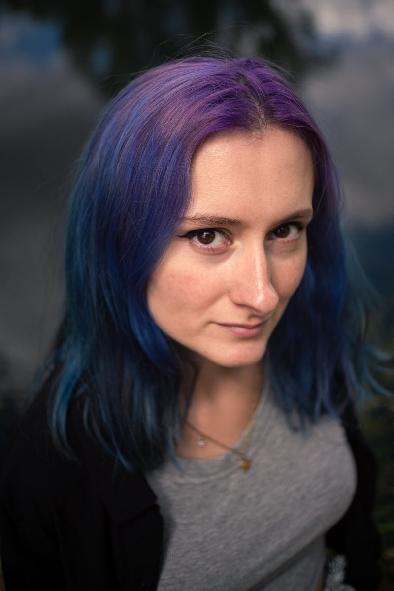 Portrait rapproché en lumière douce, cheveux violets et bleus, regard vers l'objectif