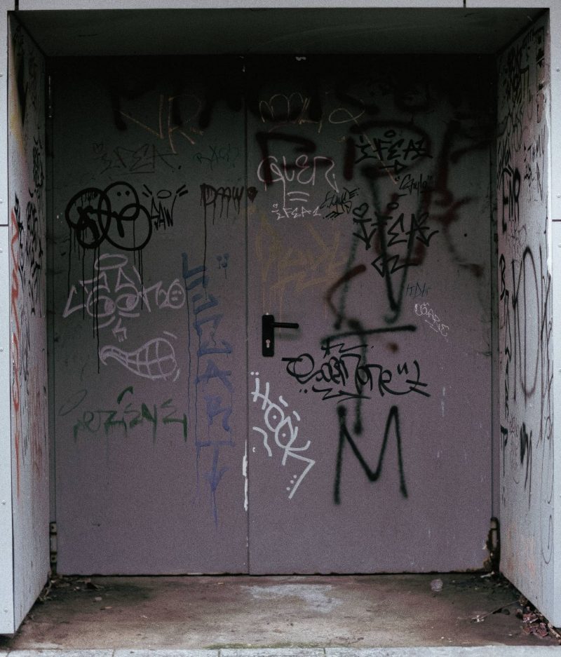 Porte métallique double couverte de graffitis, au fond d'un renfoncement de béton