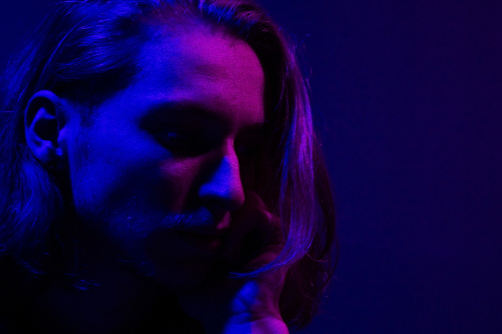 Benjamin Codoner de profil, sous une lumière bleue et violette, le regard baissé