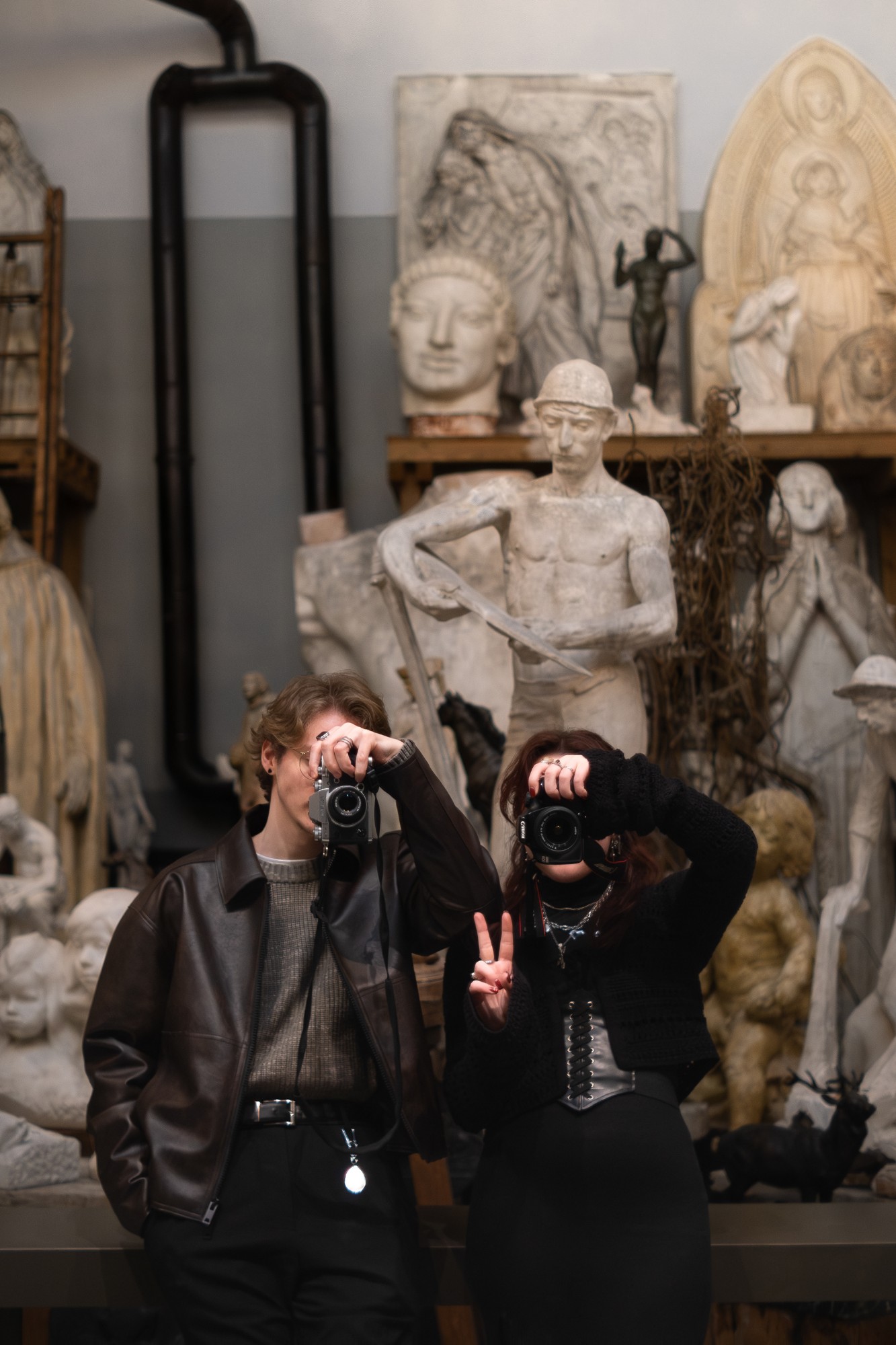 Deux photographes visant l'objectif, le visage caché par leur appareil, devant des statues en plâtre d'un atelier de sculpteur